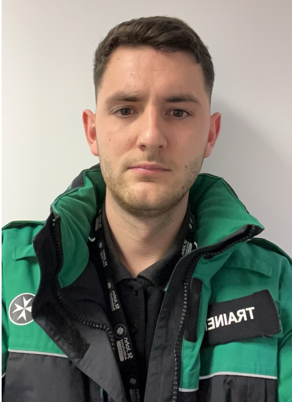 Young adult male in green St John Ambulance uniform with badge that reads 'Trainer'. Man pictured is Rory Jones.